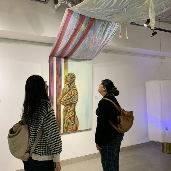 Two visitors looking up at a painting framed by a draped, hand-painted canopy