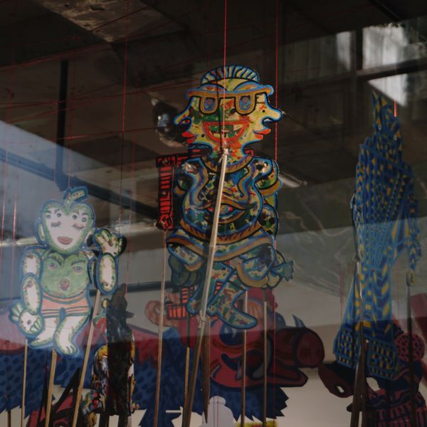 Painted wayang figures layered with reflections in the gallery glass