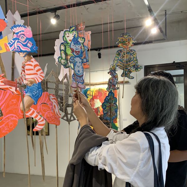A visitor playing with hand-painted wayang hanging from the ceiling