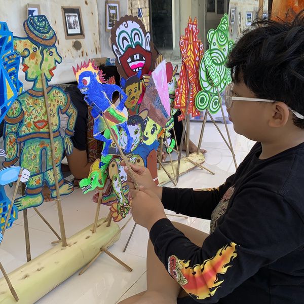 A young boy sitting on the floor, playing with a colourful bundle of handmade wayang puppets